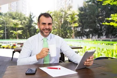 Cheerful mature businessman drinking coffee and using pc tablet