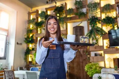 Happy waitress holding tray with cup of coffee working in cafeteria and serves the table