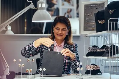 Portrait of happy elegantly dressed woman seller packs precious earrings in a box for her client in a luxury jewelry store.