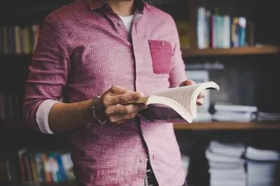 Young hipster man reading book in library.