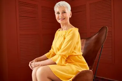 Portrait of good looking elegant middle aged Caucasian female with short blonde hair sitting comfortably in leather armchair