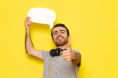 A front view young male in grey t-shirt holding white sign with smile on the yellow wall man expression emotion color model