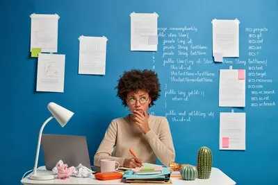 Thoughtful attractive woman in spectacles writes in diary to do list of goals, makes notes in personal organizer