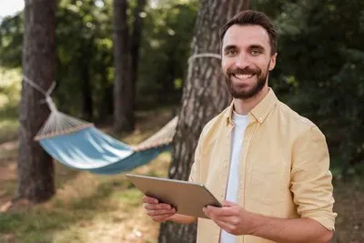 Smiley man holding tablet while camping outdoors