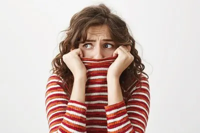 Scared timid woman looking left, shivering and hiding face inside sweater collar