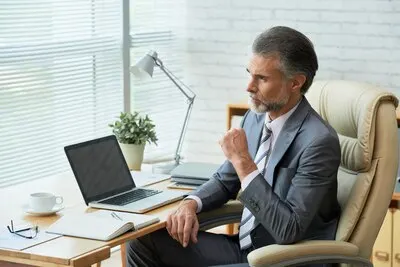 Elegant businessman at the office table looking thoughtfully at the window