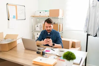 Latin business owner texting on the smartphone and updating his business social media. Young entrepreneur with an online shop