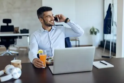 Happy businessman communicating over cell phone while having lunch break in the office