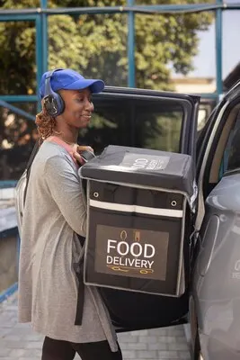 African american worker delivering meal order from the backpack by car parking in the driveway to