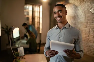 Portrait of happy black entrepreneur working late on business reports and looking at camera in the office