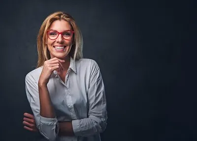 Studio portrait of blond female dressed in a white shirt and red eyeglasses.