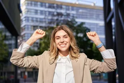 Happy smiling saleswoman in beige suit celebrates her achievement triumphing making fist pump and lo