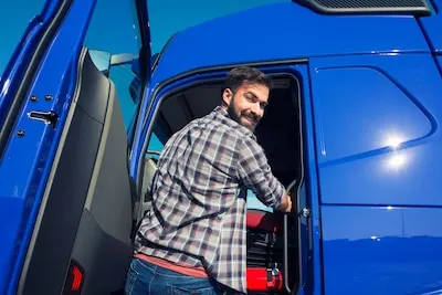 Conductor con camisa de cuadros subiendo a la cabina de un camión azul