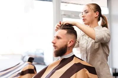 Estilista con gafas peina y corta el pelo a un cliente con barba en una peluquería