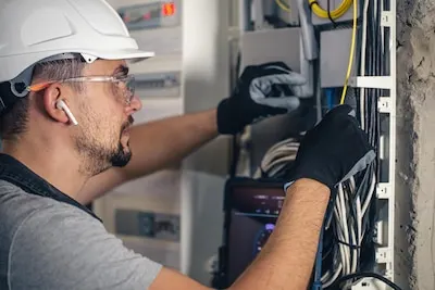 Electricista con casco y guantes trabajando en un cuadro eléctrico